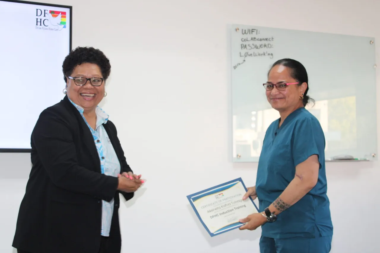 Two women smiling together, one holding a training certificate.